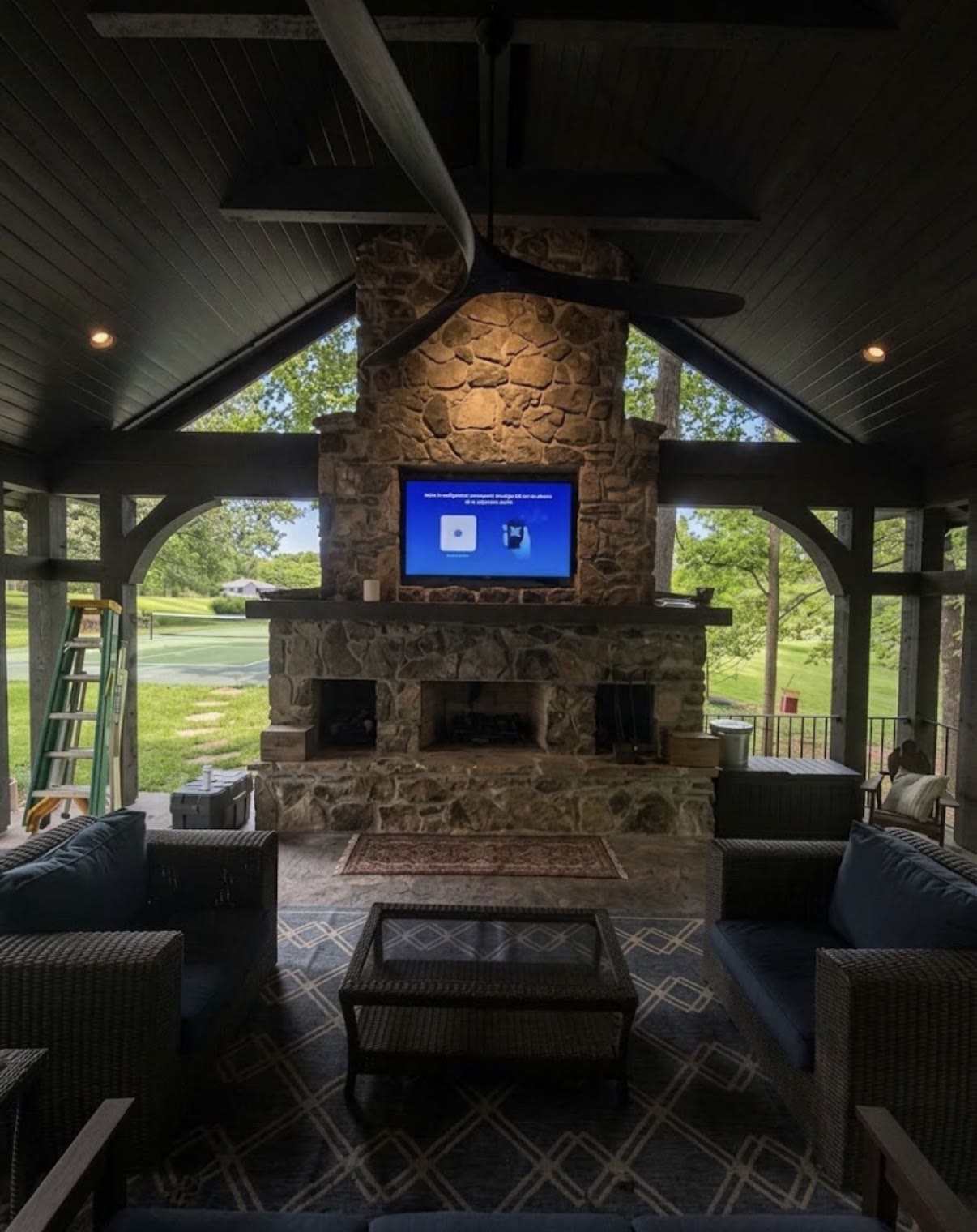 TV mounted on a stone fireplace in a covered outdoor pavilion with timber beams